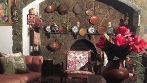 Ein gemütliches Wohnzimmer mit Kamin aus Stein, einer Couch, einem Sessel und einem Tisch mit Blumenvase.