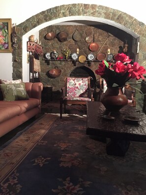 A cozy living room with a stone fireplace, a sofa, a chair, and a table with a vase of flowers. - Furnished chalet with pool and fireplace in the center of Serra Negra. (Serra Negra)