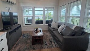 Ein Wohnzimmer mit einer Couch, einem Couchtisch, einem Fernseher und großen Fenstern.