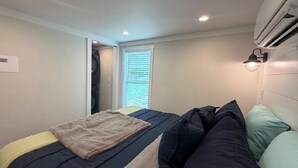 Ein Schlafzimmer mit einem Bett, einem Fenster mit Jalousien, einer Klimaanlage und einer Wandleuchte.