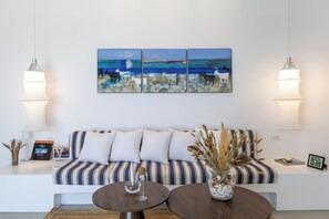 Una sala de estar moderna con un sofá a rayas, dos mesas redondas y un cuadro con motivos costeros.