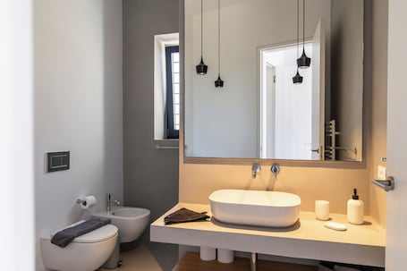 A modern bathroom with a white sink, a bidet, a toilet, and a large mirror.. Villa Nabia II, Seaview and Sunset view, Private Pool