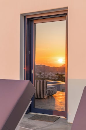 A room with a sliding glass door leading to a balcony with a view of a sunset over a cityscape. - Villa Nabia II, Seaview and Sunset view, Private Pool (Adamas)
