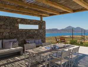 Pared de piedra, techo de madera, asientos al aire libre y una mesa con sillas y tazas.