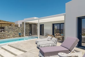 A modern outdoor pool area with lounge chairs, a stone wall, and a clear view of the sky. - Villa Nabia II, Seaview and Sunset view, Private Pool (Adamas)