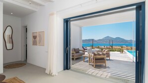 Un salón moderno con un amplio ventanal corredera que da a un balcón con piscina y vistas al mar.