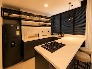 A modern kitchen with a built-in gas stove, black cabinetry, and a marble countertop. - Apartamentos HEM (Medellín)