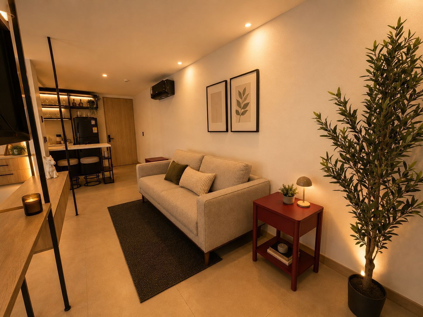 A modern living room with a sofa, a small table, a potted plant, and a kitchen area in the background.
