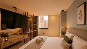 A modern hotel room with a large bed, a flat-screen TV, a wooden console table, and a city view. - Apartamentos HEM (Medellín)