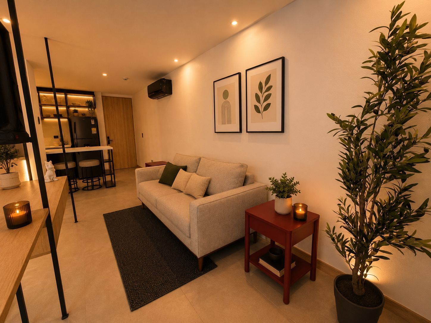 A modern living room with a sofa, a small table, a potted plant, and a kitchen area in the background.
