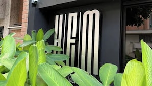 A building facade with a large, bold sign and lush green plants in front. - Apartamentos HEM (Medellín)