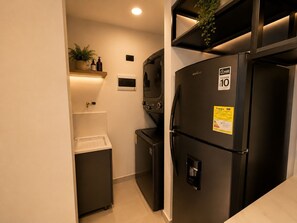Een compacte keuken met een zwarte koelkast, een klein spoelgedeelte en een plank met toiletartikelen.
