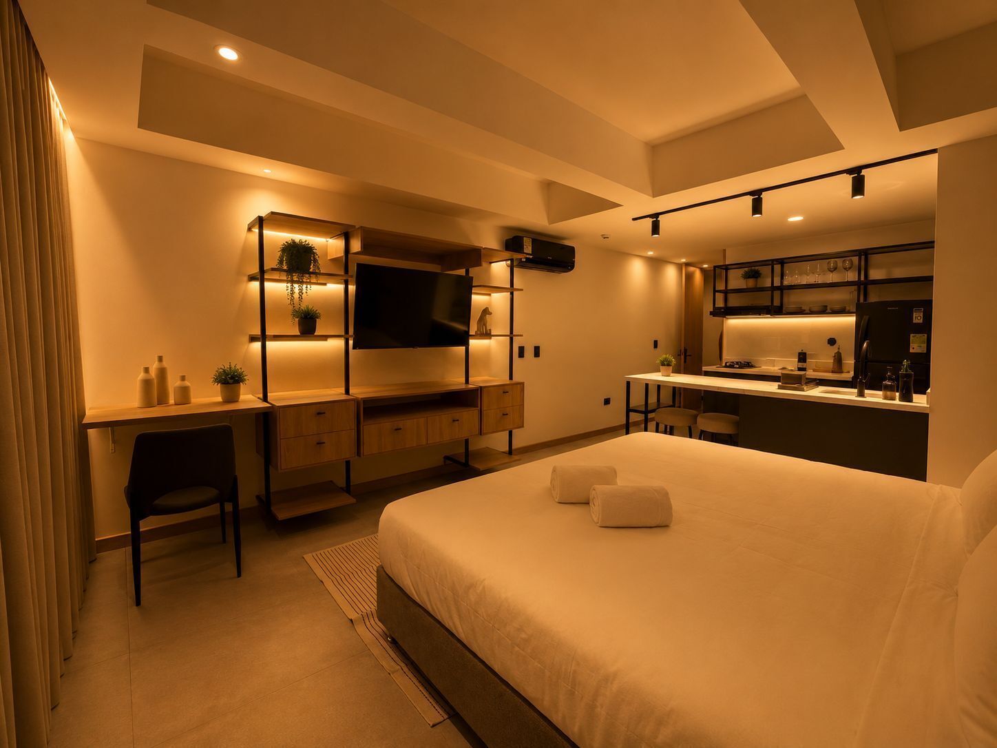Una habitación de hotel moderna con cama, escritorio, televisor y kitchenette.