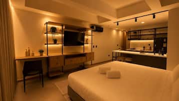 Una habitación de hotel moderna con cama, escritorio, televisor y kitchenette.