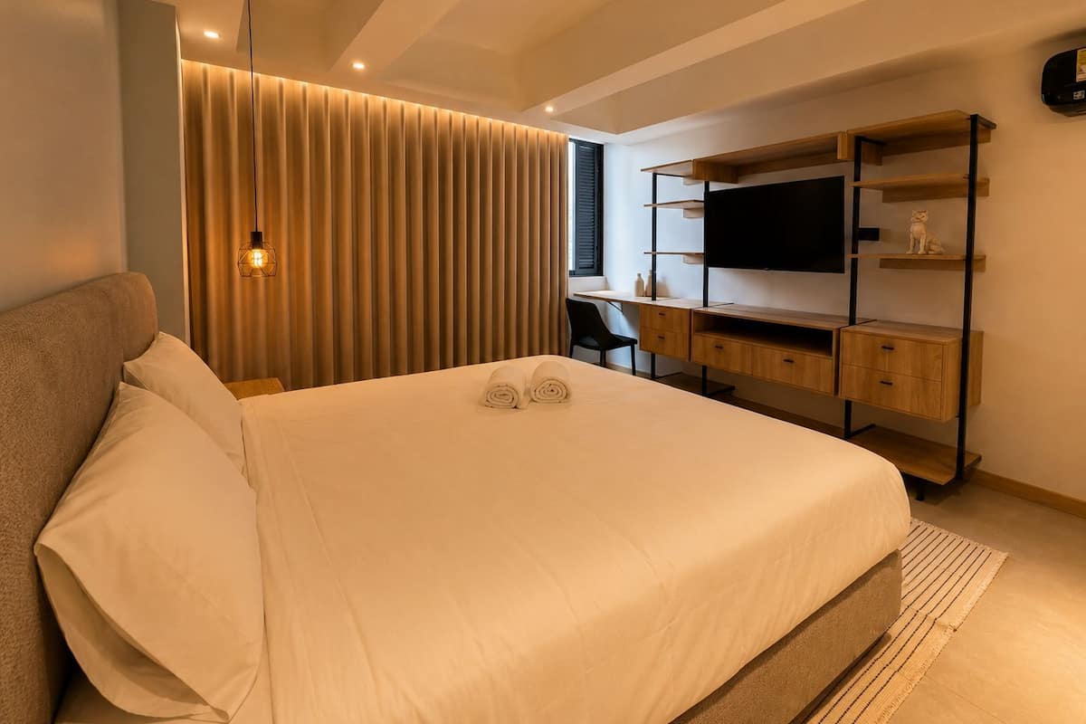 A modern bedroom with a bed, desk, and TV.