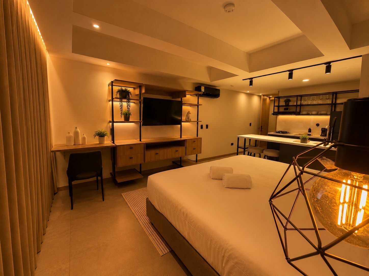 Una habitación de hotel moderna con cama, escritorio, televisor y kitchenette.