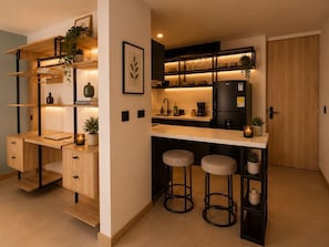 A compact kitchen with a built-in refrigerator, bar stools, and shelves with plants and kitchenware. - Apartamentos HEM (Medellín)
