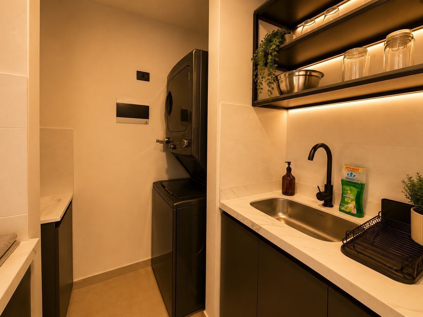 Een moderne keuken met een ingebouwde wasmachine, een roestvrijstalen spoelbak en een plank met potten en een plant.