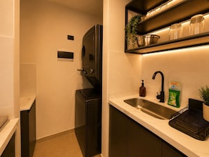 A modern kitchen with a built-in washing machine, a stainless steel sink, and a shelf with jars and a plant.