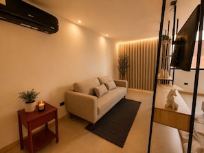 Ett modernt vardagsrum med en soffa, ett litet bord med en växt, ett ljus och en tv som står på ett tv-bord.