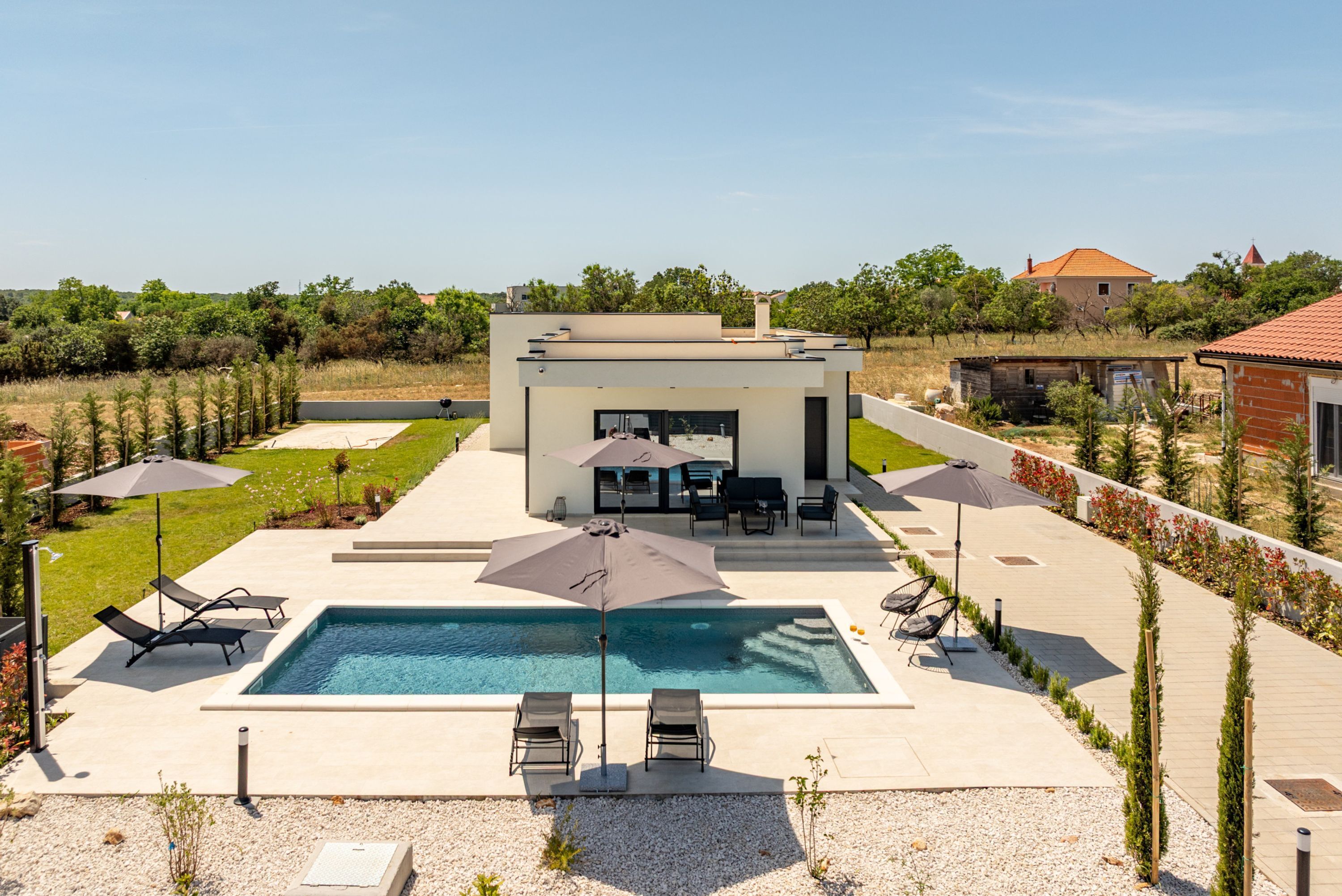 A modern outdoor pool area with lounge chairs, umbrellas, and a barbecue setup.