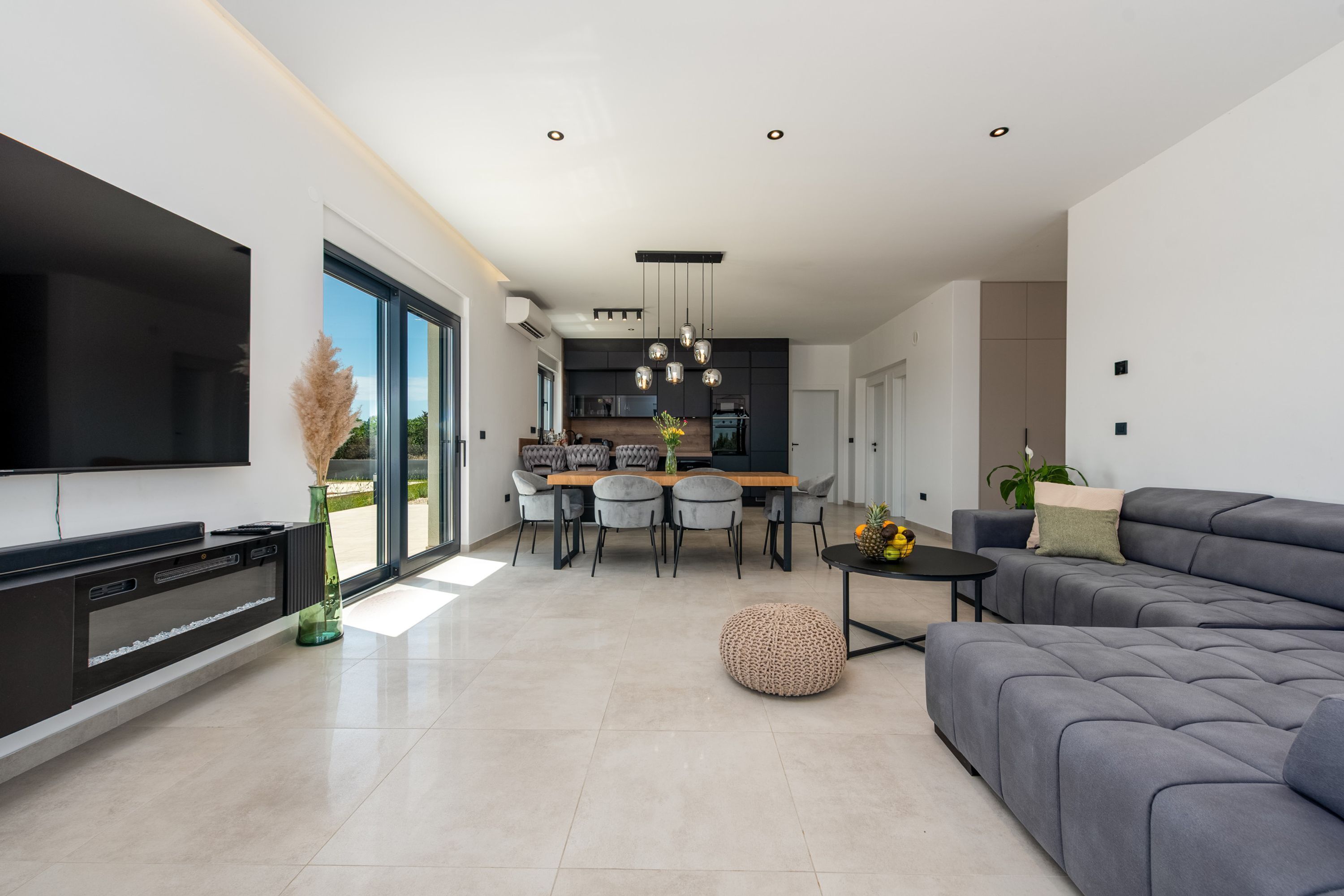 Una sala moderna con televisor de pantalla plana, sofá, comedor con sillas y cocina al fondo.
