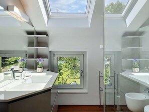 Ein modernes Badezimmer mit Dachfenstern, einem großen Fenster und Blick ins Grüne.