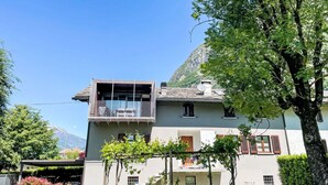 Edifici de dues plantes amb un balcó, una zona de menjador i un paisatge de muntanya de fons.