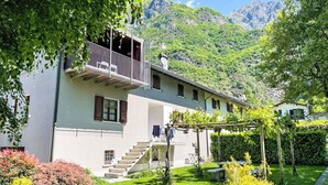 Edifici de dues plantes amb un balcó, una escala que condueix a l'entrada i un jardí amb diverses plantes.