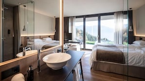 A modern hotel room with a large bed, a bathroom with a large mirror, a sink, and a view of the mountains. - Hotel Gfell (Fie allo Sciliar)