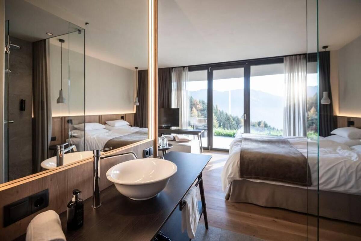 Habitación de hotel moderna con una cama grande, un baño con un espejo amplio, un lavamanos y vistas a las montañas.