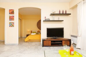 Ein Hotelzimmer mit einem Bett, einem Fernseher, einem kleinen Tisch mit Gläsern und einer Flasche sowie Bildern an den Wänden.