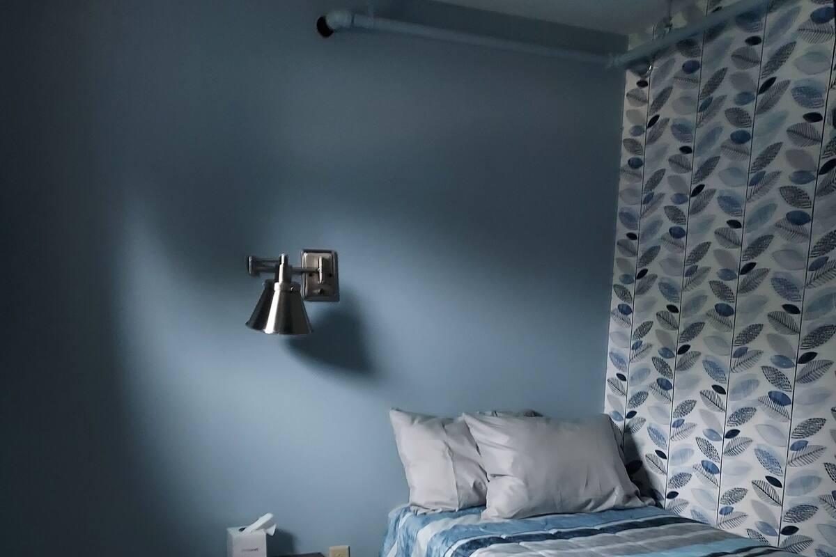 Un dormitorio con cama, mesita de noche, lámpara y cortina con estampado de hojas.