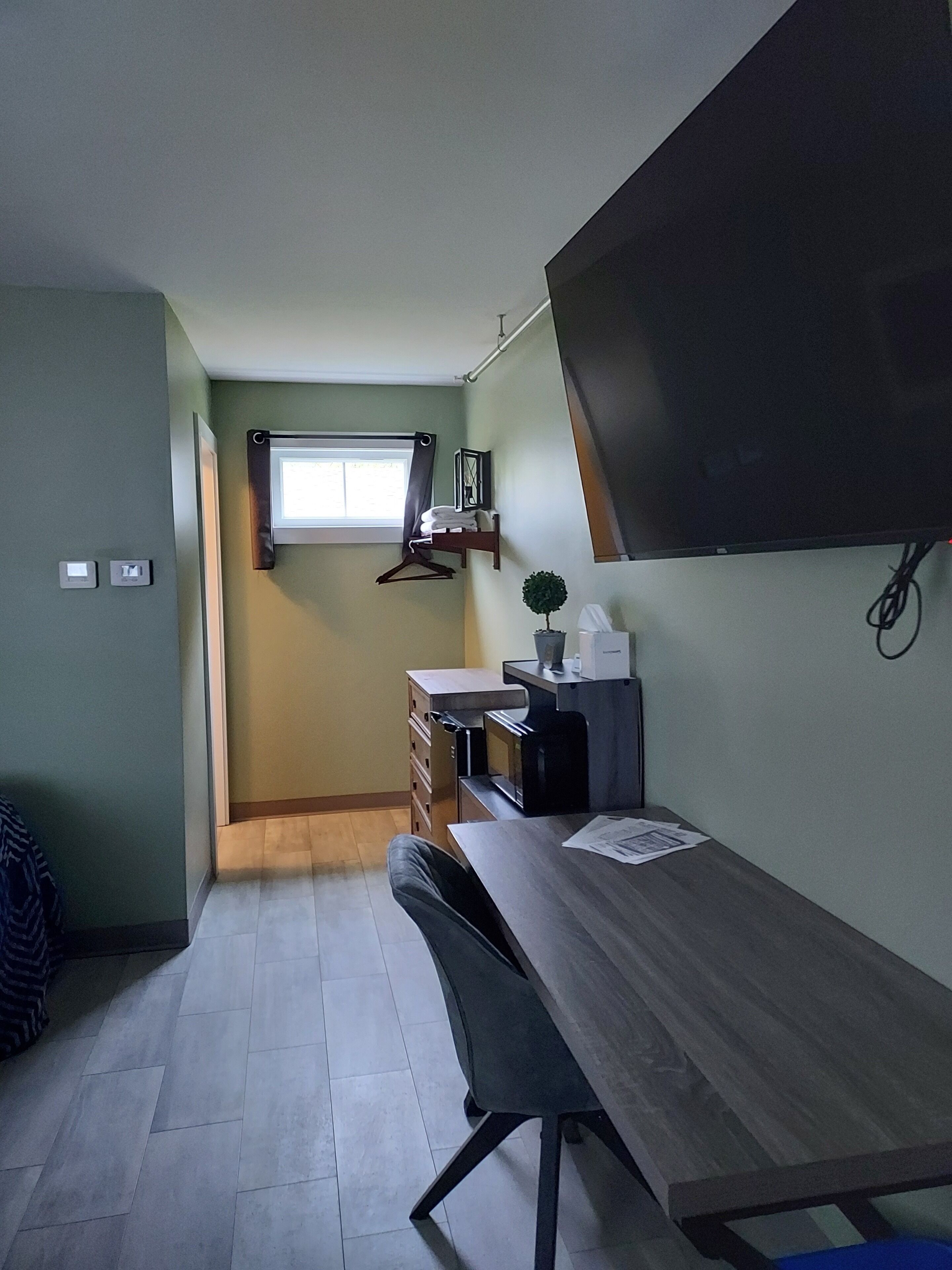 A compact room with a desk, chair, and a flat-screen TV mounted on the wall.