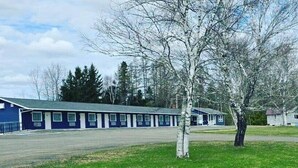 Un motel à la façade bleue, avec une enseigne indiquant « Wolastog Inn & Suites », et une zone herbeuse avec des arbres.