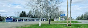 Un motel amb façana blava, un cartell de 'Wolastog Inn & Suites' i una zona verda amb arbres.