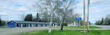 Un motel con fachada azul, un letrero que dice 'Wolastog Inn & Suites', y una zona verde con árboles.
