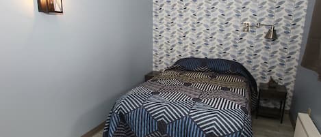 A bedroom with a bed, a wall-mounted light, a radiator, and patterned wallpaper.