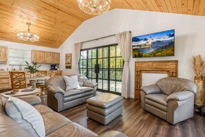 Ein großzügiges Wohnzimmer mit Ledersofas, einem Kamin und einem großen Fenster mit schöner Aussicht.