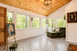Ein Zimmer mit Holzbalkendecke, großen Fenstern, einem grünen Sofa und einem gemusterten Boden.