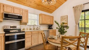 Une cuisine avec des meubles en bois, des appareils électroménagers en acier inoxydable, une table à manger avec des chaises et une fenêtre avec des rideaux.