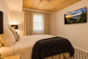 Ein Schlafzimmer mit Bett, Vorhängen, einem Gemälde und einer Holzbalkendecke.