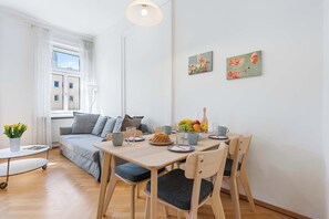 A modern living room with a sofa, a dining table with chairs, a small round table, and a window with curtains. - Bright Apartment | Kitchen | Well Connected (Wien)