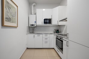 A modern kitchen with white cabinets, a microwave, a coffee maker, and a gas stove. - Design 3BR Apartment | Comfort | Kitchen | Central (Wien)
