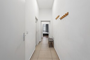 Un couloir étroit aux murs blancs, avec un banc et un présentoir en bois.