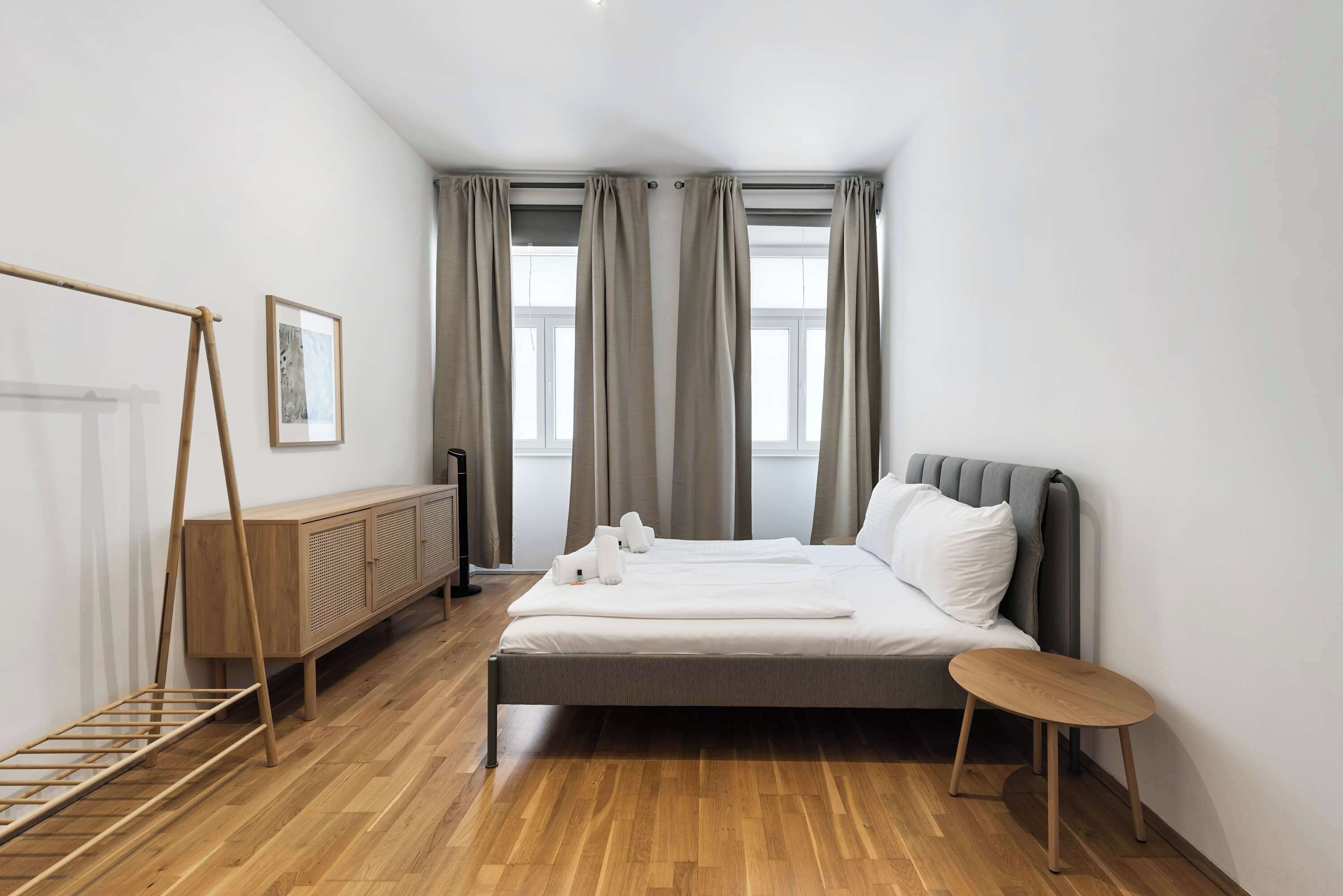 A modern hotel room with a bed, a wooden floor, a radiator, a picture on the wall, and a window with curtains.