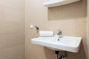 Ein Badezimmer mit einem weißen Waschbecken, einem Handtuch und einem Lichtschalter an der Wand.