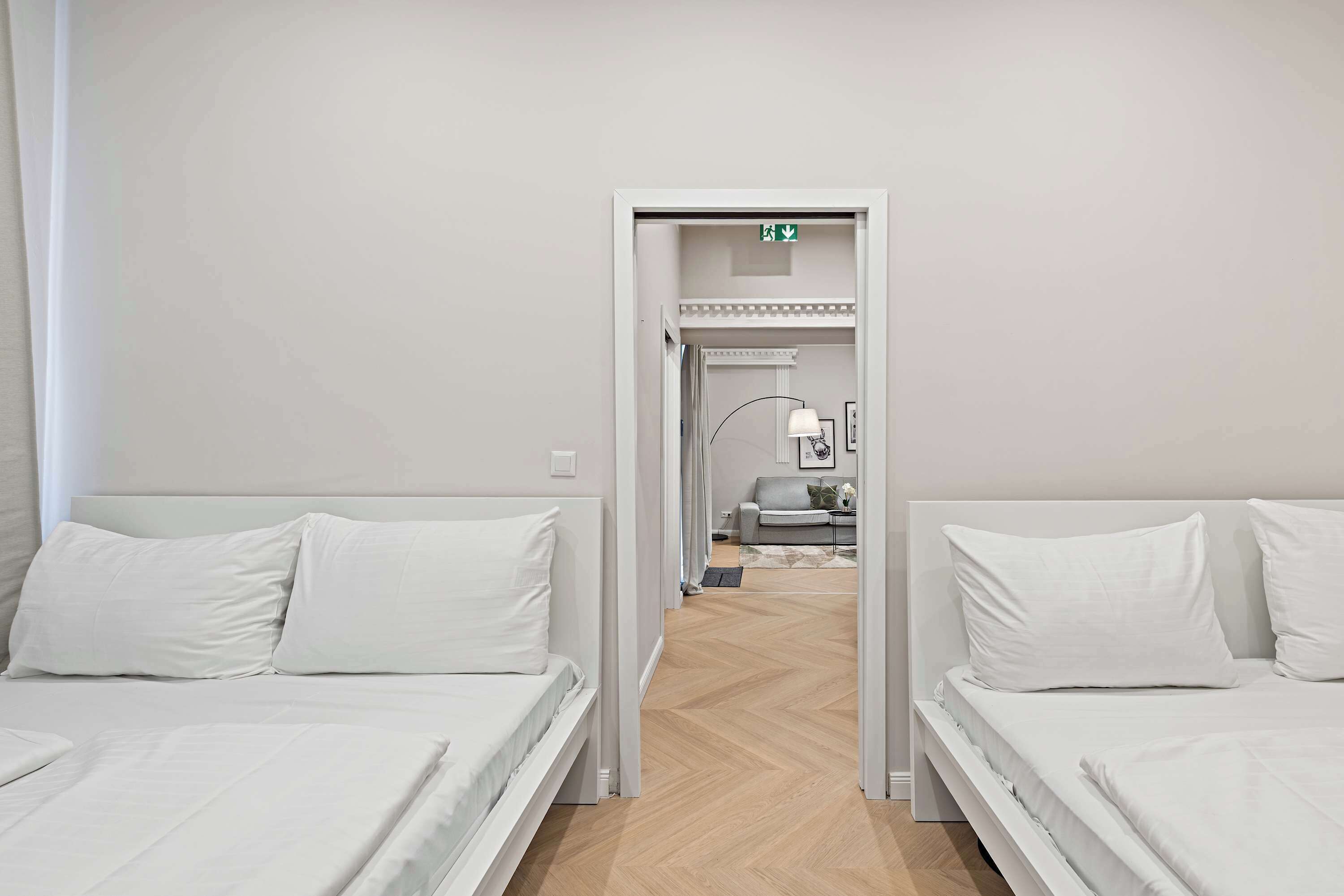 A hotel room with two beds, a hallway leading to a bathroom, and a small sitting area with a sofa and table.