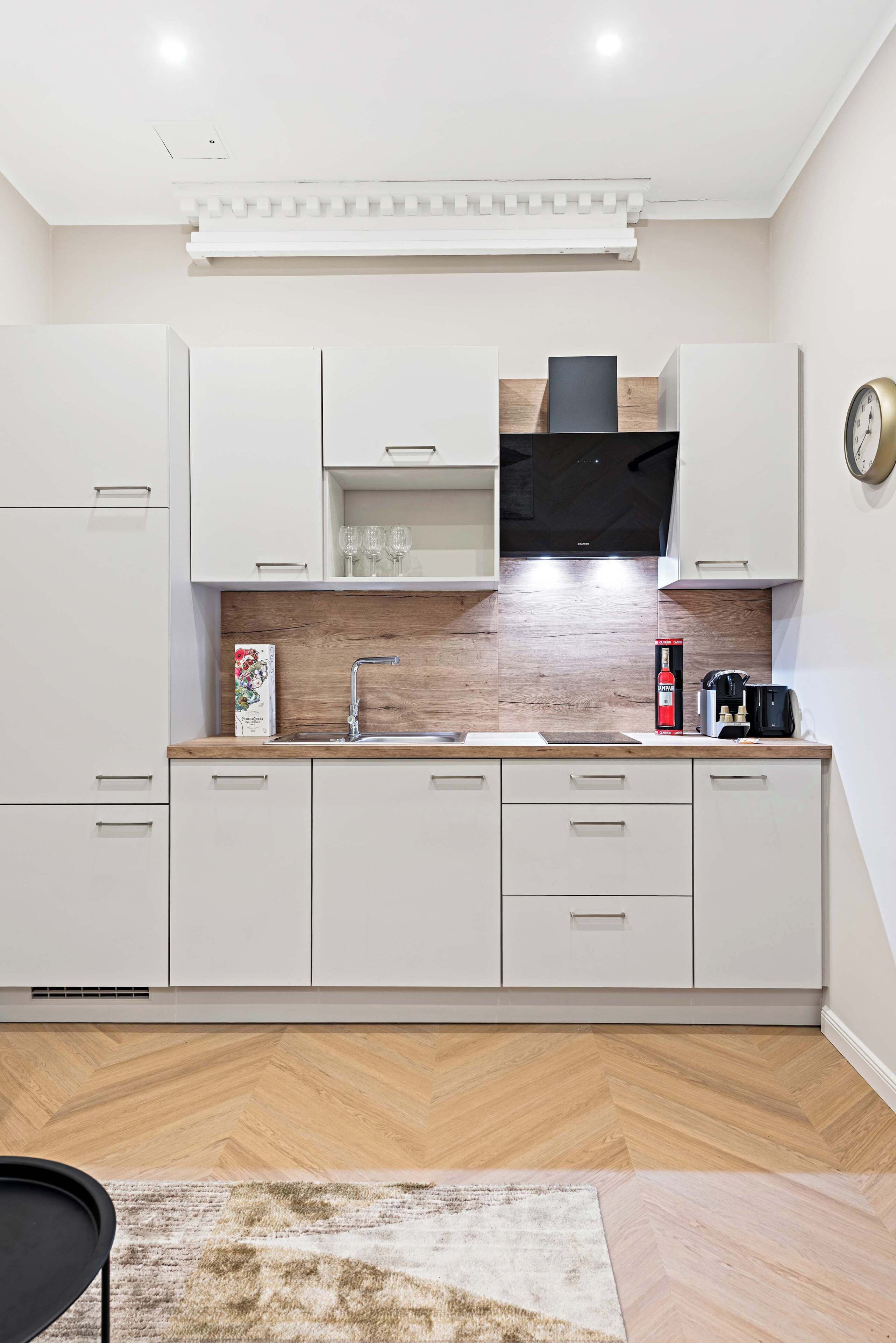 Una cocina moderna con armarios blancos, piso de madera en espiga y microondas integrado.