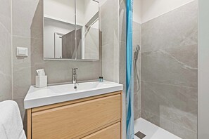 A bathroom with a white sink, wooden vanity, a mirror, and a shower curtain. - Kaiser Apartment 2BR | Metro | Kitchen | Central (Wien)